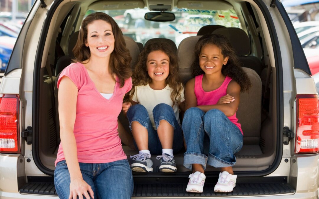 Woman, two young girls sitting in back of van smiling