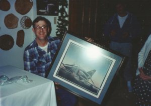 A man seated at a table holding a framed picture