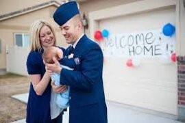 A man in dress uniform holding an infant with a woman standing next to him.