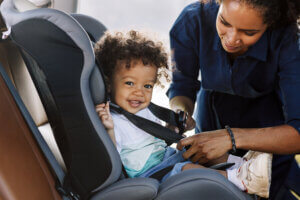 Toddler in a car seat smiles while his mother buckles him in